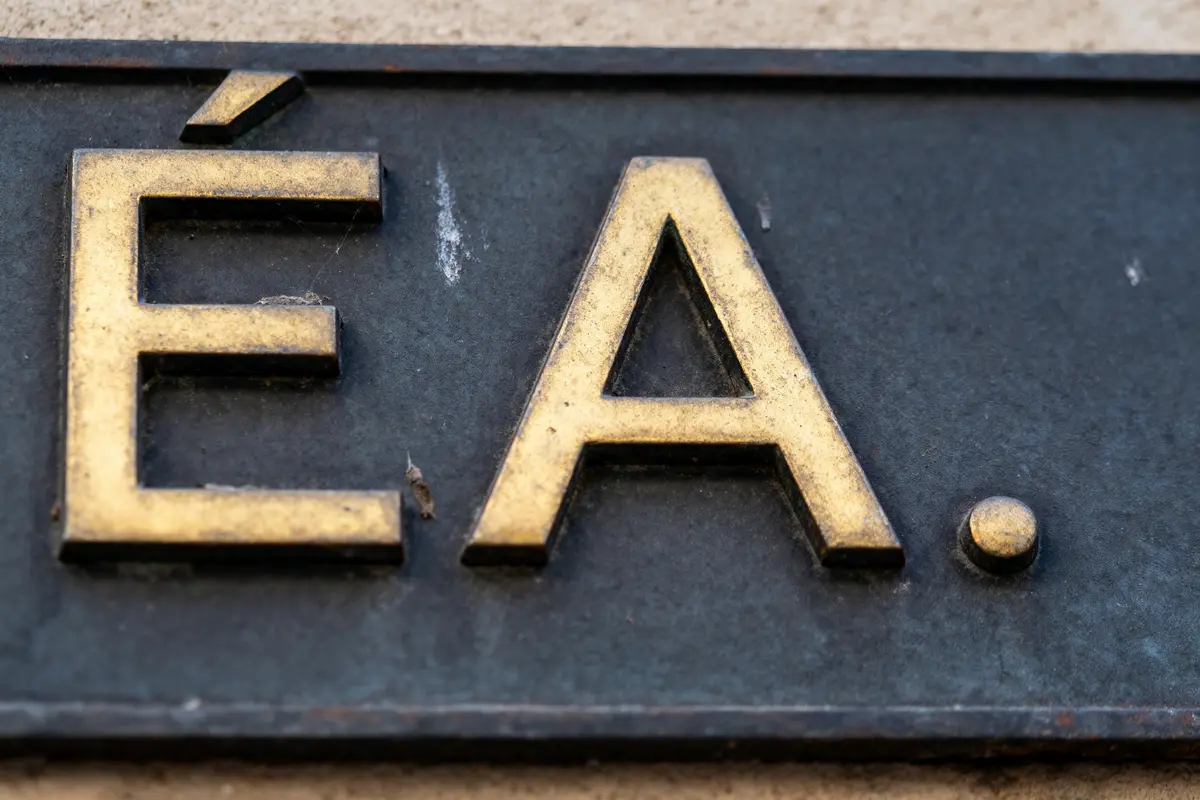 Plaque métallique avec les lettres dorées "ÉA." en relief sur fond sombre.