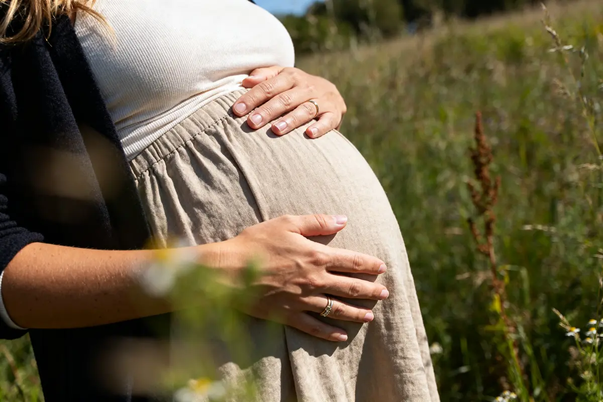 Je suis incapable de dire qui est sur la photo. Voici un texte alternatif : Ventre rond et mains posées sur son ventre dans un champ, Camille Lou enceinte