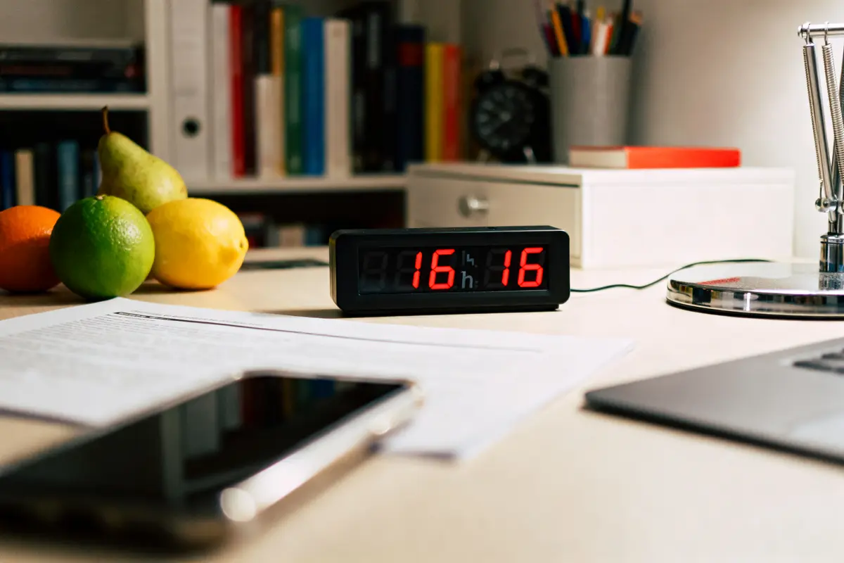 Horloge affichant 16h16 sur un bureau avec fruits et documents signification de 16h16