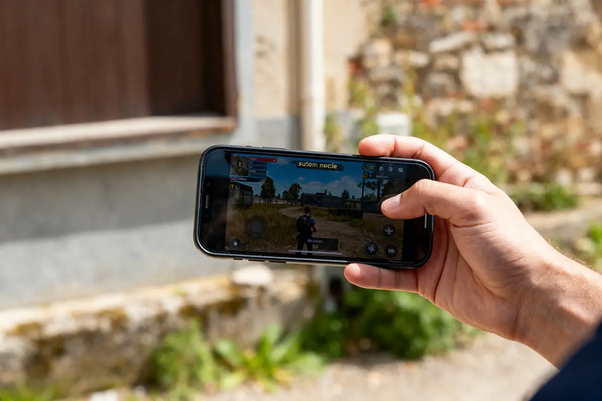 Une main tenant un smartphone affichant un jeu vidéo avec sutom nocle.