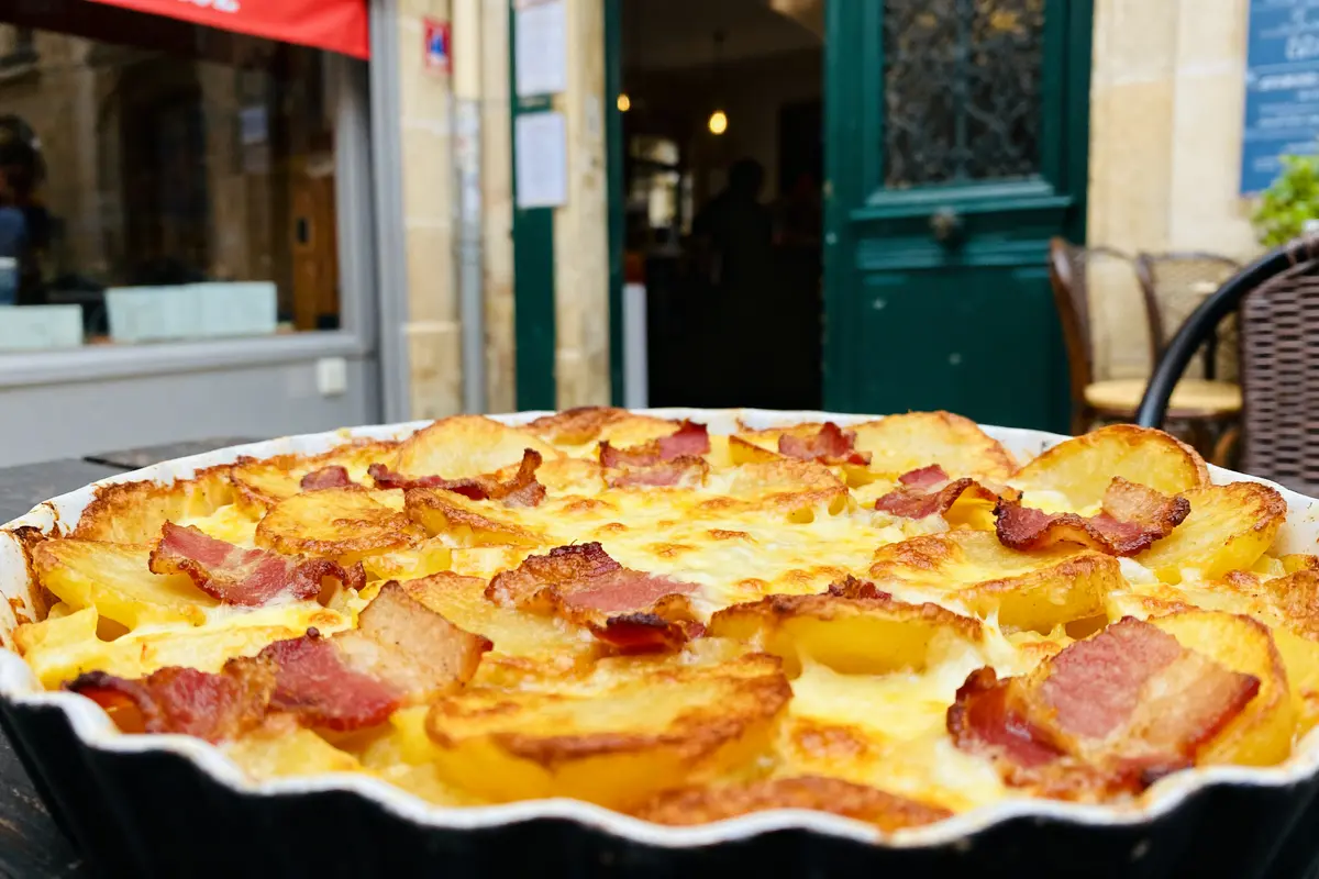 Plat de tartiflette enceinte avec lardons et fromage devant un restaurant français