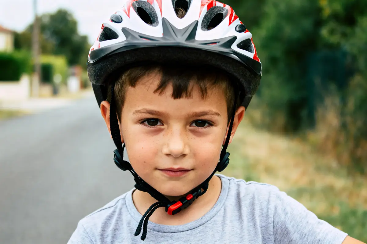 Enfant portant un casque enfant rouge et blanc sur une route floue en arrière-plan