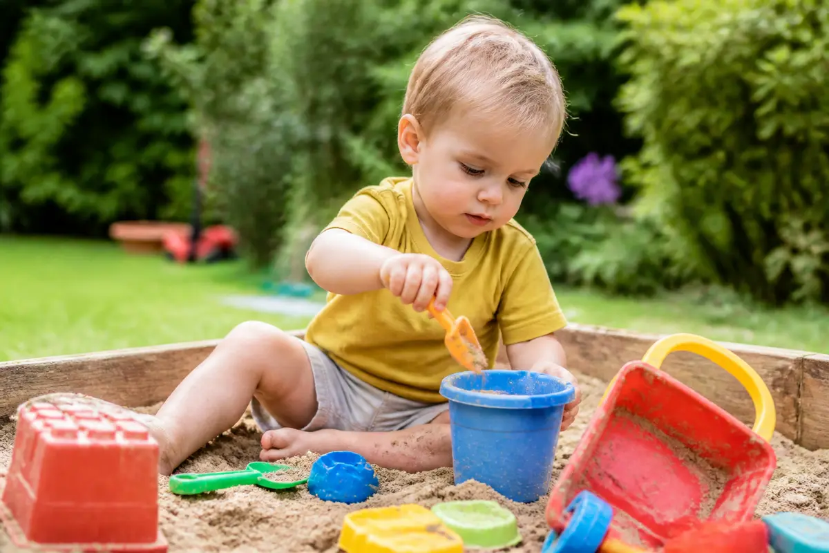 Enfant de 2 ans jouant avec des jouets colorés dans le sable à l'extérieur