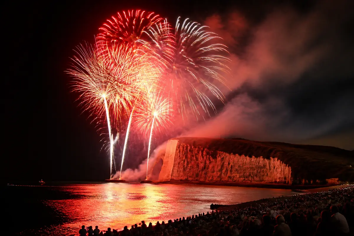 Feu d'artifice Étretat 2025 illuminant la falaise et la mer avec foule enthousiaste