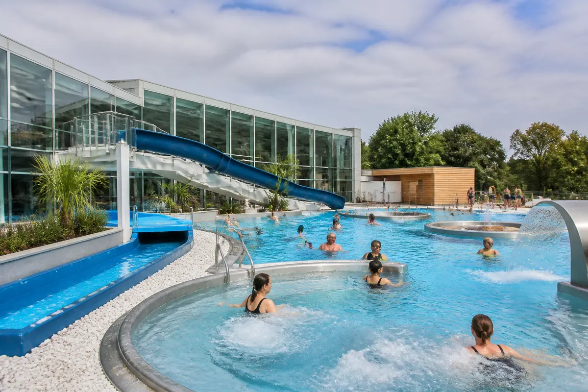 Personnes profitant d'une piscine extérieure à Lille avec toboggan et jets d'eau relaxants
